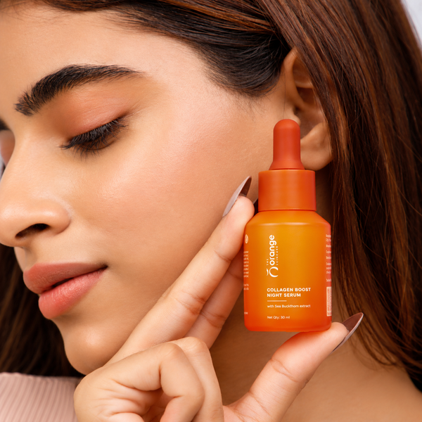 A close-up lifestyle shot of a woman holding an orange dropper bottle of 'Orange' brand Collagen Boost Night Serum next to her face.