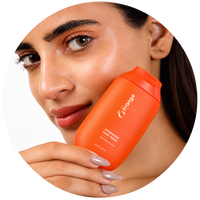 A close-up of a woman holding an orange bottle of hydrating face wash against a white background, framed in a circular crop.